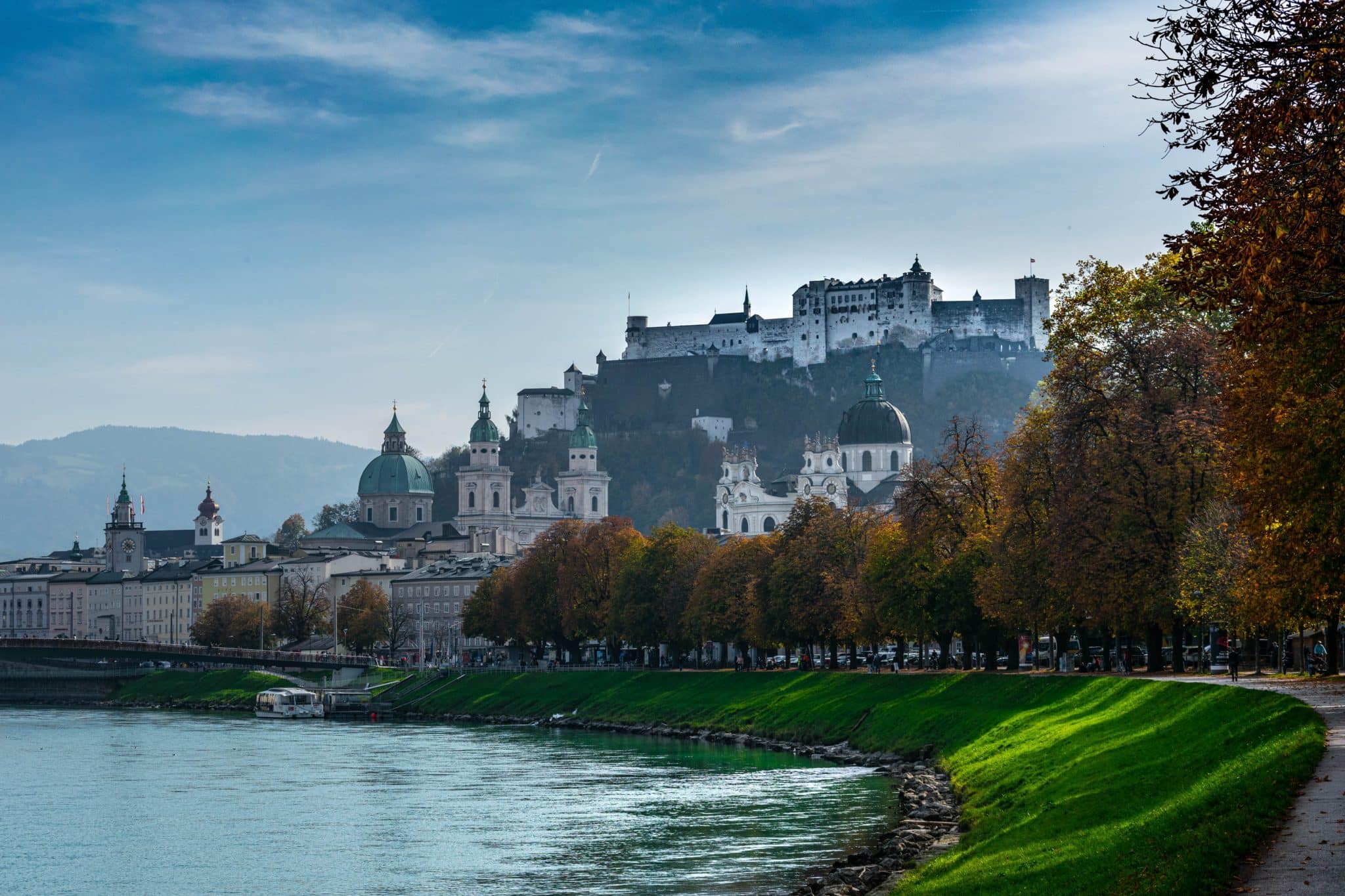 a river with trees and buildings on top of it with Salzburg in the background