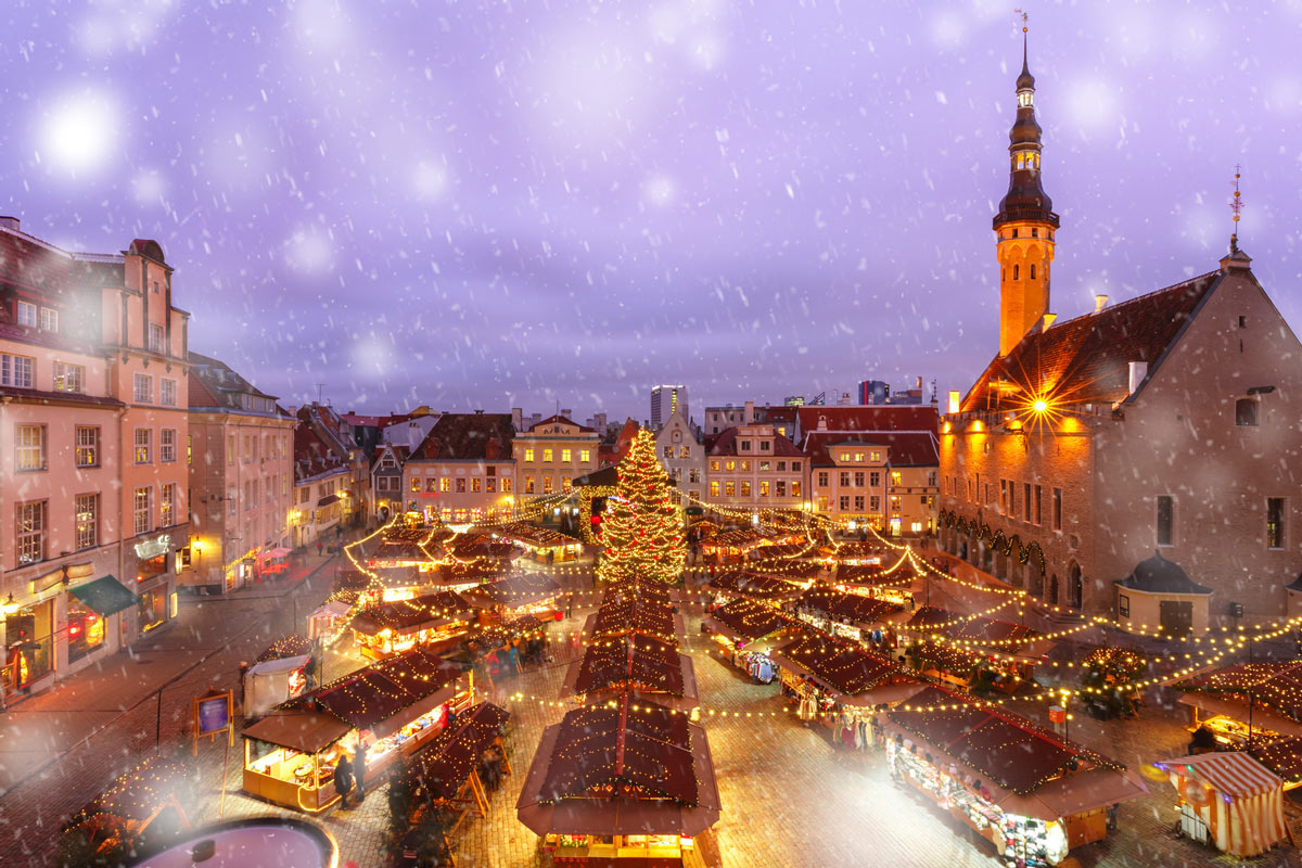 A magical aerial view of Tallinn Christmas Market in Estonia, with twinkling lights and soft snowflakes falling, capturing the charm of luxury Christmas travel to European Christmas markets.